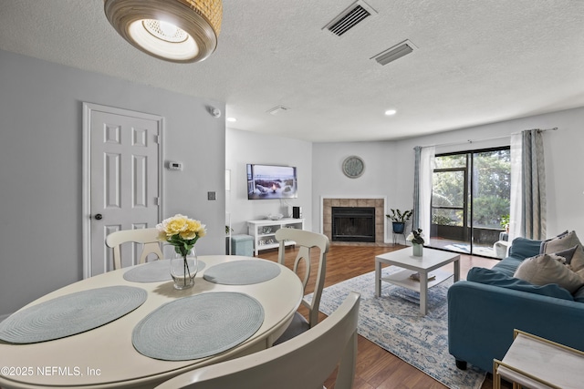 dining room featuring visible vents, a textured ceiling, wood finished floors, and a fireplace