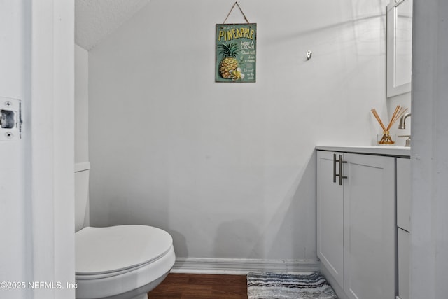 half bath with baseboards, toilet, vanity, wood finished floors, and a textured ceiling