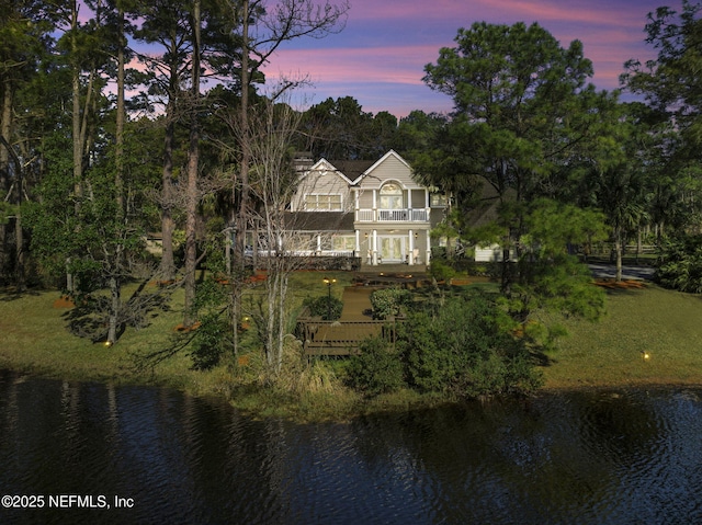 back of house at dusk featuring a water view and a balcony