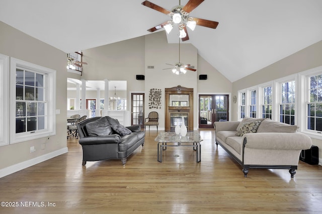 living area with high vaulted ceiling, visible vents, baseboards, light wood finished floors, and ornate columns