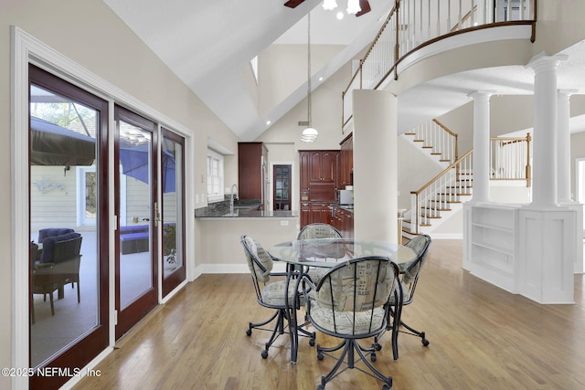 dining space with arched walkways, decorative columns, light wood finished floors, high vaulted ceiling, and stairs