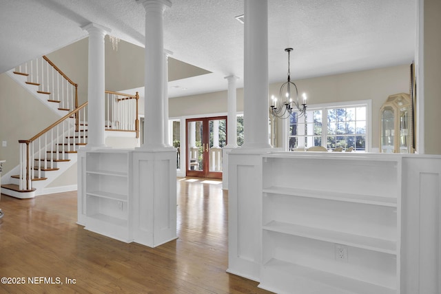 interior space with ornate columns, a textured ceiling, wood finished floors, and an inviting chandelier