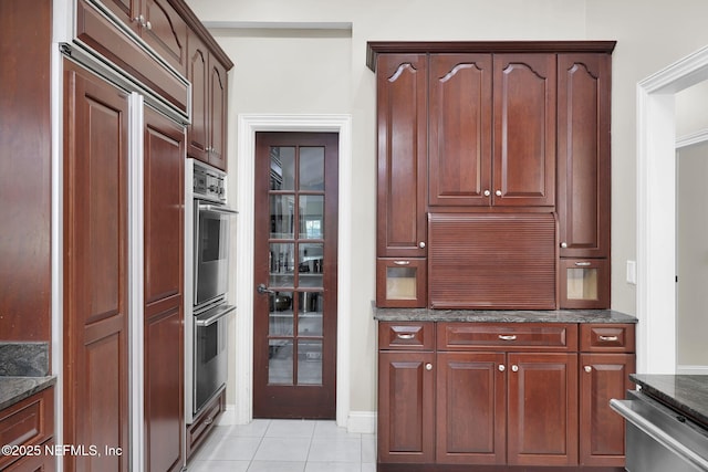 kitchen with appliances with stainless steel finishes, light tile patterned flooring, and dark stone countertops