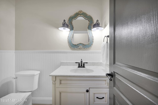 half bath with wainscoting, vanity, and toilet