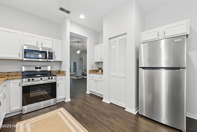 kitchen with appliances with stainless steel finishes, dark stone counters, white cabinetry, and dark wood-style floors