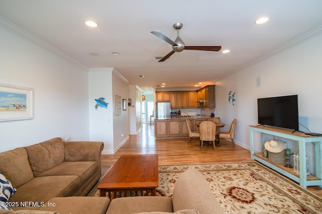 living room featuring baseboards, a ceiling fan, ornamental molding, light wood-style floors, and recessed lighting