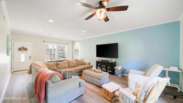 living area with a textured ceiling, ornamental molding, light wood-style flooring, and baseboards