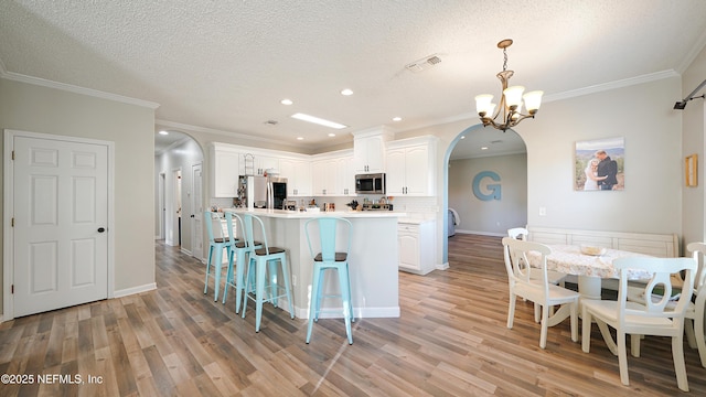 kitchen with arched walkways, decorative light fixtures, stainless steel appliances, light countertops, and white cabinetry