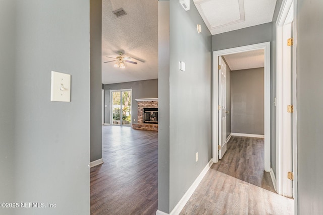 corridor featuring visible vents, a textured ceiling, baseboards, and wood finished floors