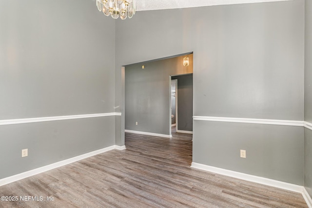 empty room featuring baseboards, wood finished floors, a chandelier, and a towering ceiling