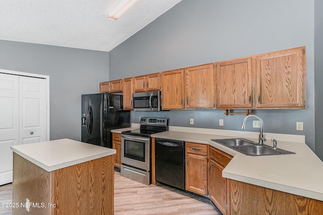 kitchen with light wood finished floors, black appliances, light countertops, a textured ceiling, and a sink