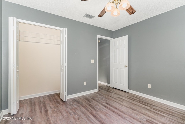 unfurnished bedroom featuring visible vents, ceiling fan, baseboards, wood finished floors, and a textured ceiling