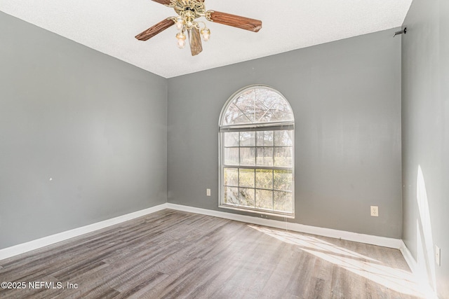 empty room with a textured ceiling, baseboards, a ceiling fan, and wood finished floors