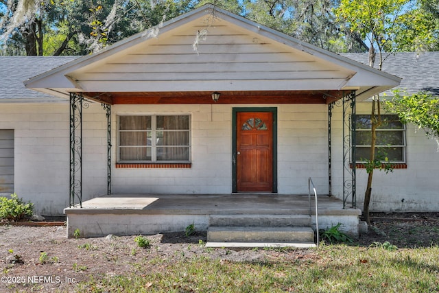 bungalow-style house with a shingled roof, a porch, and concrete block siding