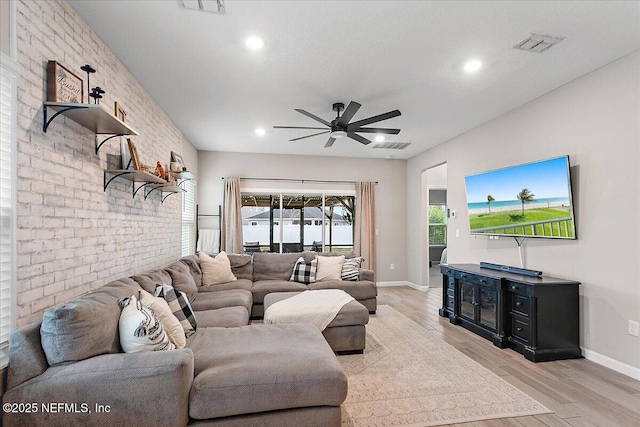 living area featuring visible vents, baseboards, brick wall, ceiling fan, and light wood-type flooring