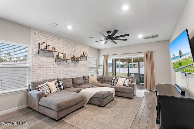 living area featuring a textured ceiling, a ceiling fan, visible vents, and light wood-style floors