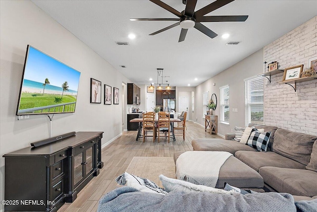 living area featuring light wood-type flooring, baseboards, visible vents, and a ceiling fan