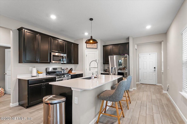 kitchen featuring decorative light fixtures, a kitchen island with sink, stainless steel appliances, light countertops, and a sink