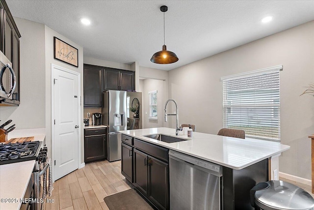 kitchen featuring pendant lighting, light countertops, appliances with stainless steel finishes, a kitchen island with sink, and a sink