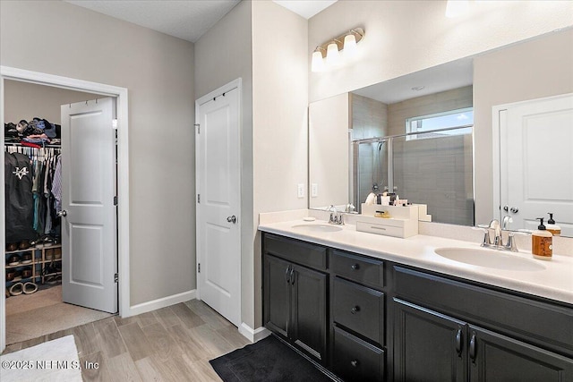 full bathroom with a spacious closet, double vanity, a stall shower, and a sink