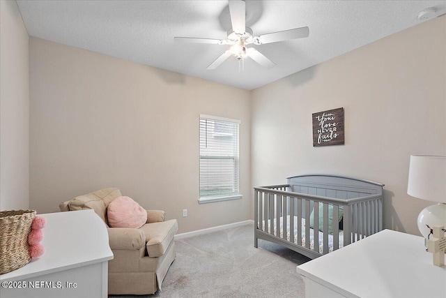 bedroom with light carpet, baseboards, a ceiling fan, a textured ceiling, and a nursery area