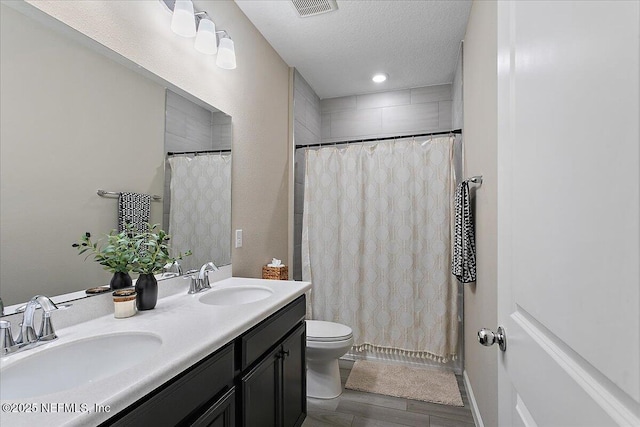 full bathroom with a textured ceiling, double vanity, a sink, and visible vents