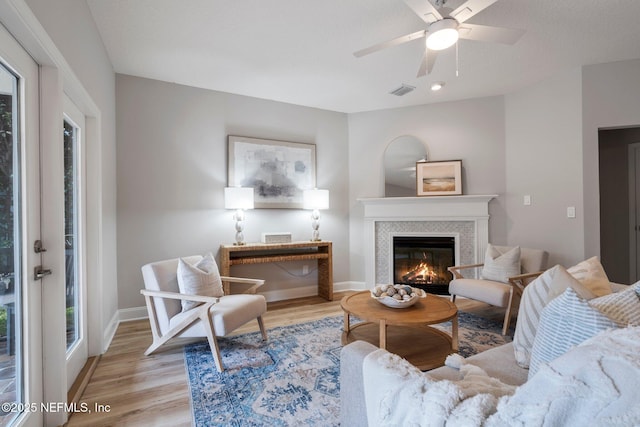 living room featuring visible vents, a ceiling fan, light wood-type flooring, baseboards, and a tile fireplace