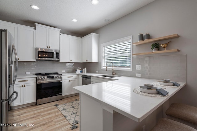 kitchen with a breakfast bar area, appliances with stainless steel finishes, a peninsula, light countertops, and a sink