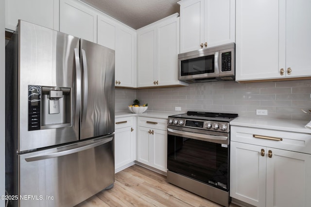 kitchen featuring light wood finished floors, appliances with stainless steel finishes, light countertops, and decorative backsplash