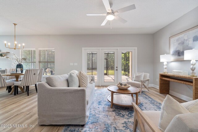 living area featuring baseboards, a textured ceiling, french doors, light wood-style floors, and ceiling fan with notable chandelier