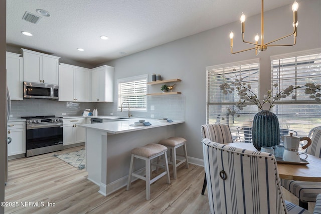 kitchen with visible vents, decorative backsplash, appliances with stainless steel finishes, light wood-type flooring, and a sink