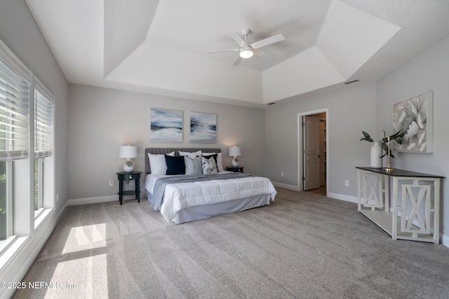 carpeted bedroom with ceiling fan, a raised ceiling, visible vents, and baseboards