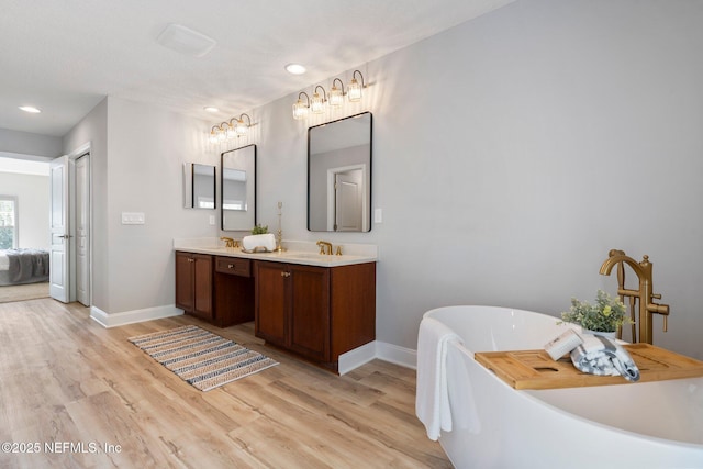 ensuite bathroom with double vanity, a sink, wood finished floors, a freestanding tub, and baseboards