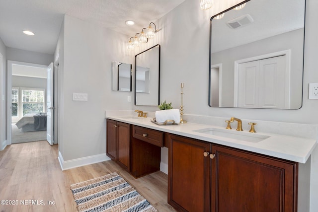 ensuite bathroom featuring double vanity, wood finished floors, a sink, and visible vents