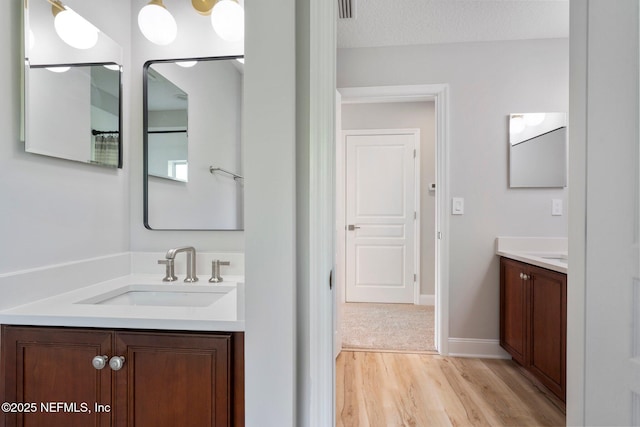 full bath with visible vents, baseboards, wood finished floors, a sink, and two vanities