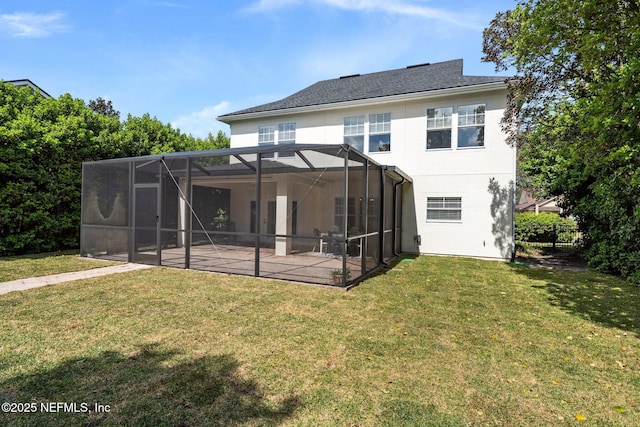 rear view of house with a yard, glass enclosure, a patio, and stucco siding