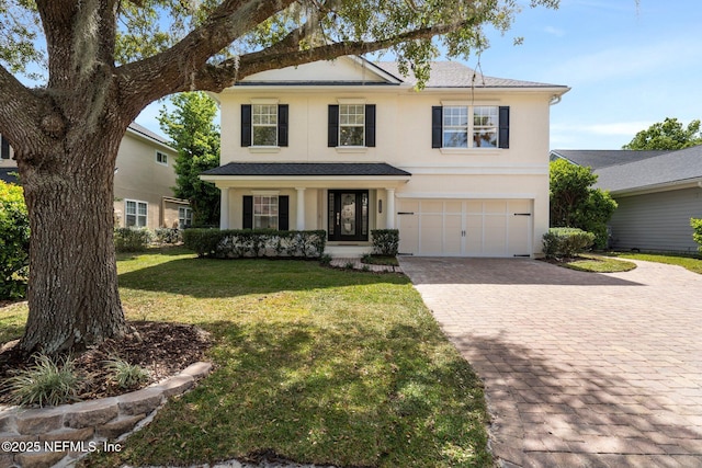 traditional-style house featuring a garage, decorative driveway, a front yard, and stucco siding