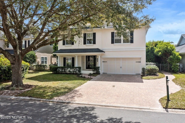 traditional home with an attached garage, fence, decorative driveway, and stucco siding