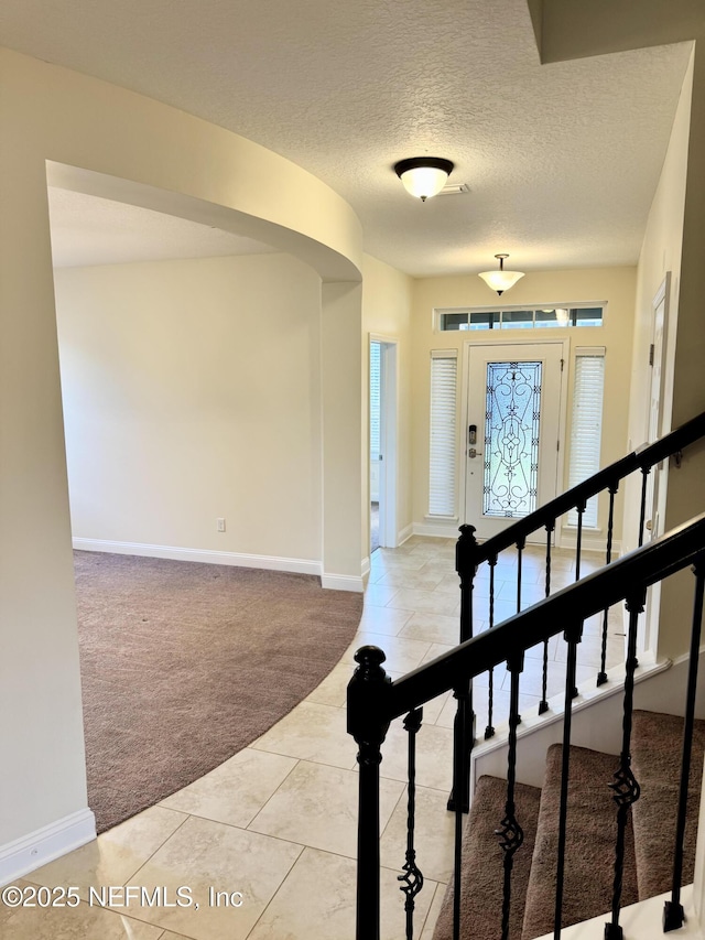 foyer with light colored carpet, a textured ceiling, baseboards, and stairs