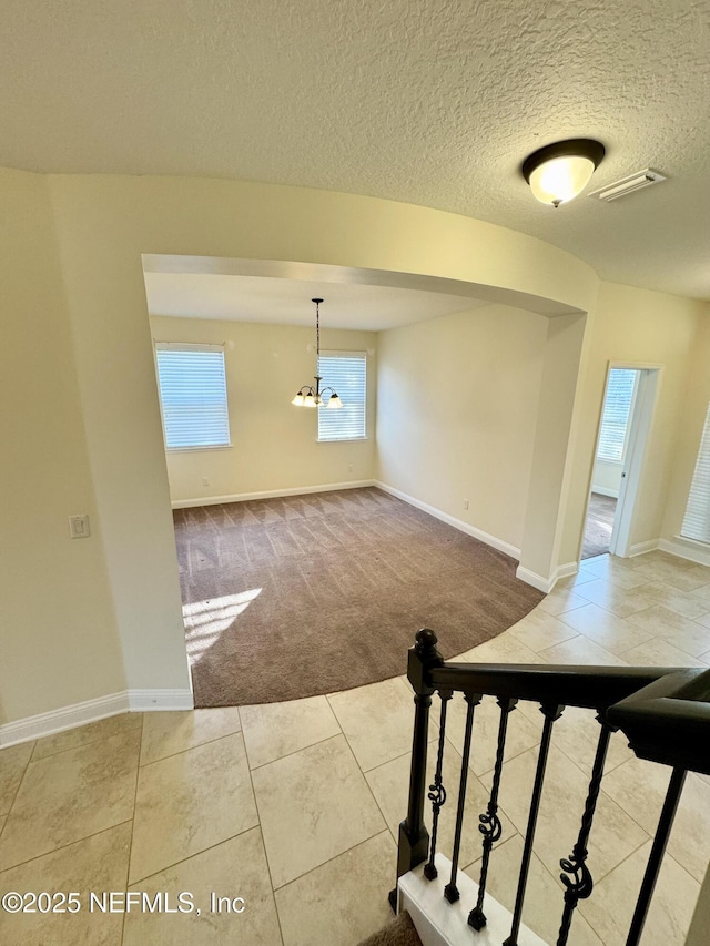 unfurnished room featuring baseboards, visible vents, light colored carpet, a textured ceiling, and a chandelier