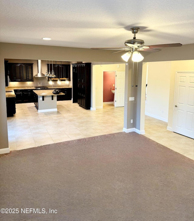 kitchen with dark cabinets, light carpet, a breakfast bar, open floor plan, and wall chimney range hood