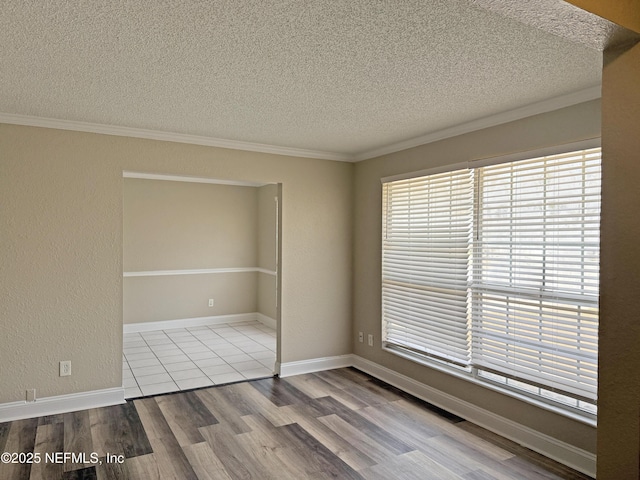 spare room featuring a textured ceiling, a textured wall, wood finished floors, baseboards, and ornamental molding