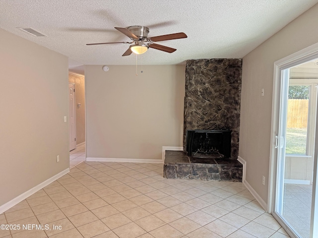 unfurnished living room with a textured ceiling, ceiling fan, a stone fireplace, light tile patterned flooring, and visible vents