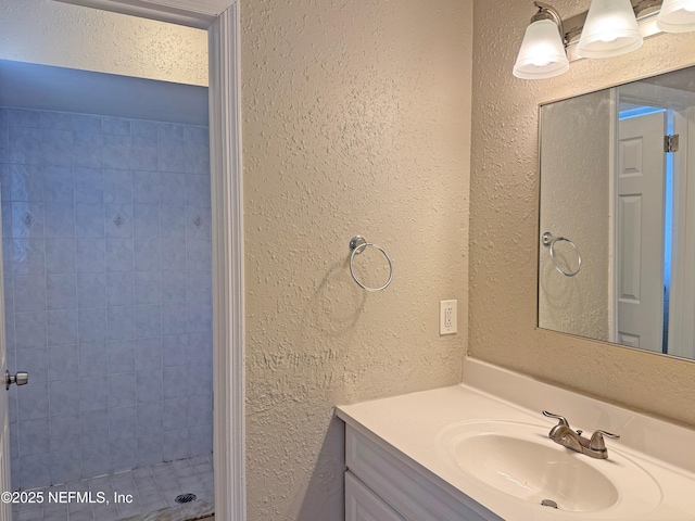 full bath with vanity, a tile shower, and a textured wall