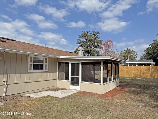 rear view of property with roof with shingles, a chimney, fence, and a sunroom