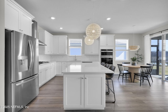 kitchen with appliances with stainless steel finishes, white cabinetry, wall chimney exhaust hood, and wood finished floors