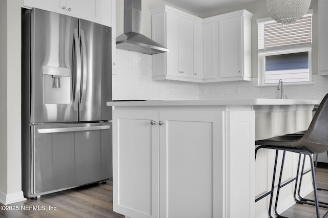 kitchen featuring light wood-style floors, light countertops, wall chimney range hood, white cabinetry, and stainless steel refrigerator with ice dispenser