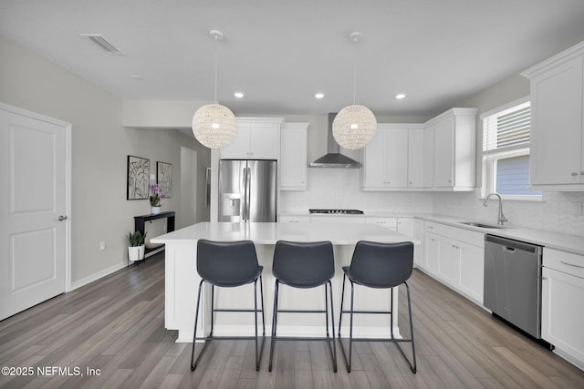 kitchen with stainless steel appliances, a kitchen island, a sink, visible vents, and wall chimney range hood