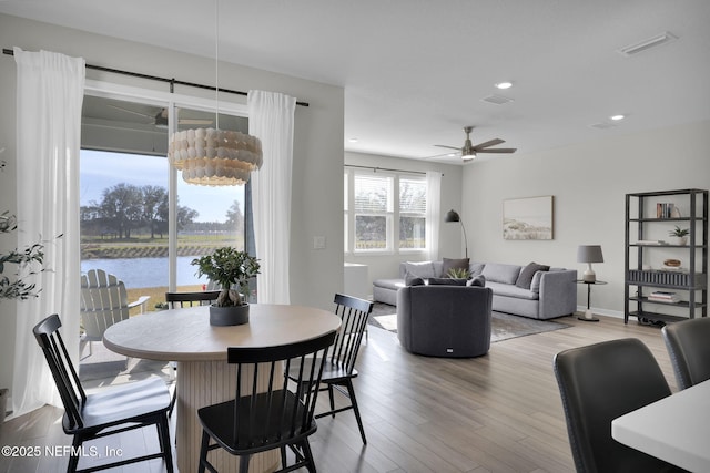 dining area featuring recessed lighting, visible vents, a water view, and wood finished floors