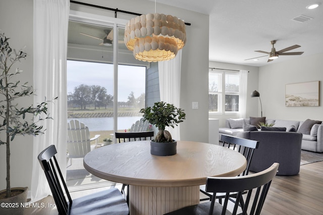 dining room with recessed lighting, a water view, wood finished floors, visible vents, and a ceiling fan